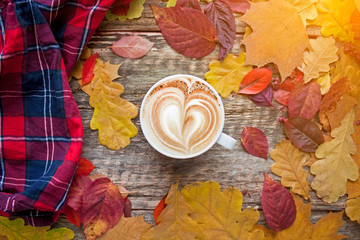 A cup of coffee with cappuccino and autumn leaves on old wooden background. Autumn decor, fall mood, autumn still life.