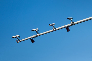 Four CCTV cameras mounted on the mast of the road post. All 4 cameras are looking in the same direction for watching the road traffic & people safety. Absolutely clear blue sky is on background