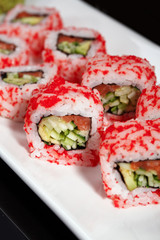Salmon and caviar rolls are served on a white plate.