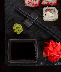 Japanese Traditional Cuisine. A set of sushi is served with chopsticks and soy sauce on black slate, decorated with wasabi and ginger.