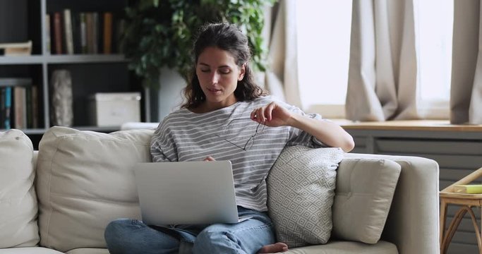 Millennial woman using laptop computer thinking of new remote work opportunities, choosing or doubting on online services sitting on sofa. Young lady doing internet research making decision at home.