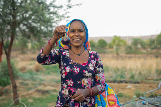 woman holding brinjal and smiling, in the field
