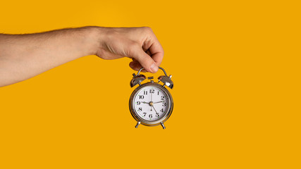 Meeting deadlines and scheduling. Millennial guy holding alarm clock on orange background, closeup....