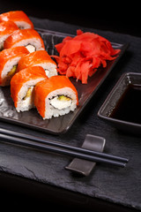 Sushi roll with salmon, avocado and cheese laid out on a black plate. Sushi menu.