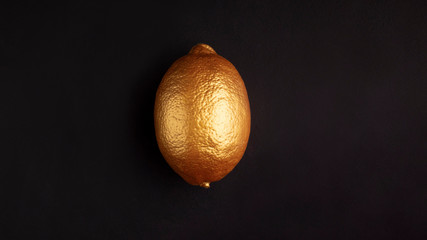 Lemon in gold paint isolated on black background.