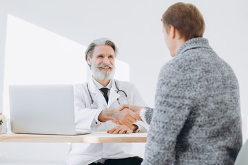Senior doctor shaking hands with patient while meeting at doctor's office.