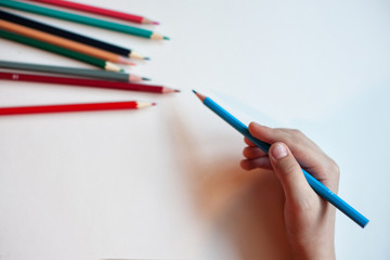 A child with a pencil in his hand Colored pencils on a background of white and colored paper. Colorful pencil on a white background. Children use these pencils as home activities and applications.