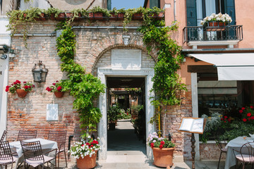 Italian typical street. Bright wall and window. Cafe on the street in Venice, Italy. Nobody in sunny day. Summer time. Ancient building. Table and flower pot in restraurant. Relax and coffe break.