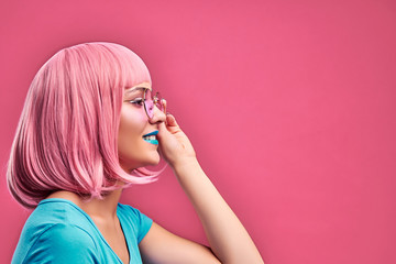 Beautiful retro-style girl with pink hairstyle, in a blue T-shirt and touching pink glasses on a pink background