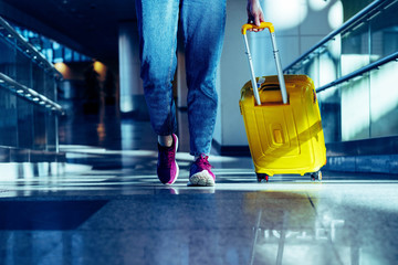 Obraz premium Women's legs close up in casual clothes walking with a yellow suitcase at the airport