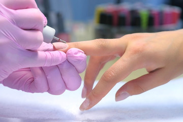Manicure master doing manicure for client using electric nail file drill machine, hands closeup...