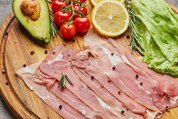 Italian prosciutto crudo or spanish jamon. Raw ham on stone cutting board decoreted with spices, lettuce, lemon, tomatoes and avocado
