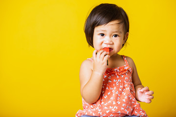 Happy portrait Asian baby or kid cute little girl attractive laugh smile playing holds cut watermelon fresh for eating, studio shot isolated on yellow background, healthy food and summer concept