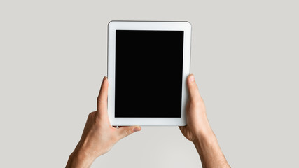 Closeup of young man holding tablet computer with empty screen on light background. Mockup for design. Panorama