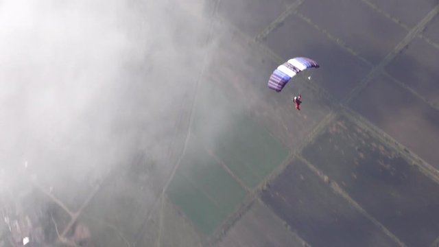 Skydiver pilots its parachute in the sky among the clouds.