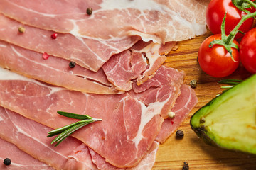 Italian prosciutto crudo or spanish jamon. Raw ham on stone cutting board decoreted with spices, lettuce, lemon, tomatoes and avocado