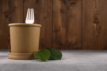 Cardboard soup container with green leaves is a motivating concept of ecology on a wooden background. Mock-up. Copy space. The concept of ecology.