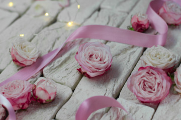 
Pink roses with satin ribbon and backlight on a background of gray bricks