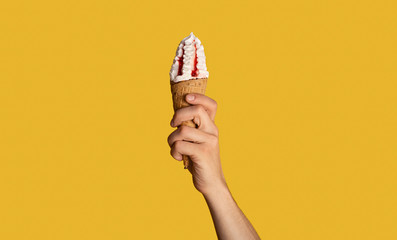 Millennial guy holding tasty ice cream with fruit topping in waffle cone, orange background,...