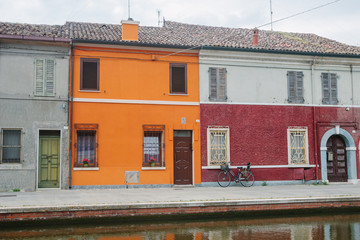 Italian street and bright orange house and water canal. Evetyday life. Inside of yard. Nobody. Middle day in Italy. Walking around in little town. Courtyard in house. Commachio.