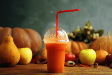 Glass of pumpkin juice placed on a wooden table near the apples and pumpkins.