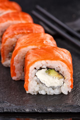 Beautiful sushi roll topped with salmon stuffed with cream cheese on a black stone board.