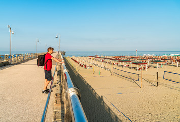 Man with backpack looks at the sea from the beach bridge.
