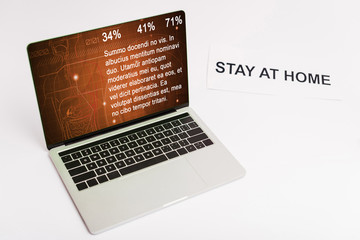 laptop with medical website on screen near paper with stay at home lettering on white