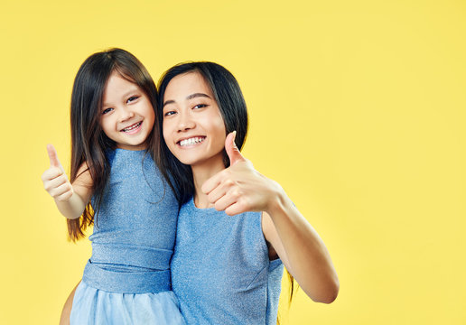 Happy mother and her child daughter showing thumbs up on yellow background