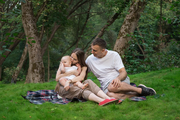 Young parents with little children having picnic in summer. Mom dad and baby sitting on picnic blanket