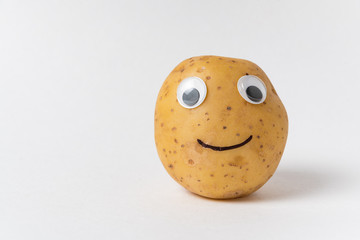 Funny raw potatoes with Googly eyes and smile on white background. Food with funny face