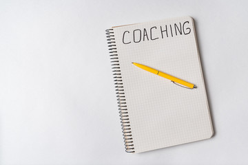 COACHING, word written on notebook, white background. Top view of notepad and pen. Copy space