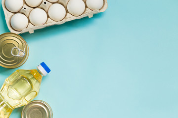 Food product donations, oil bottle, chicken eggs and canned food isolated on blue background