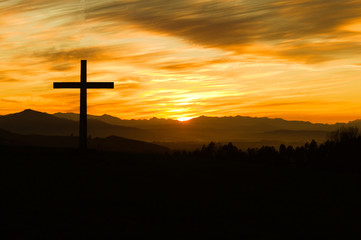 Silueta de cruz cristiana sobre atardecer con montañas al fondo