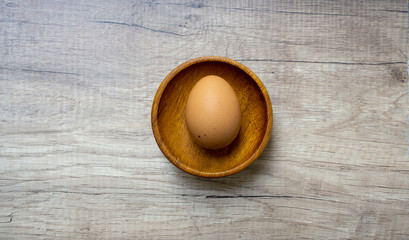 Brown chicken hen egg in brown wooden bowl on wooden table, top view angle of shooting with copy space