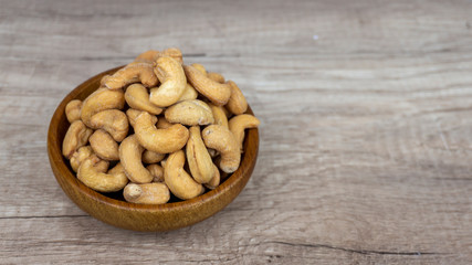 A pile brown seeds of cashew nut roasted with salt in wooden bowl on wooden table, top view angle of shooting with copy space