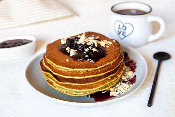 Pancakes with blueberry jam and nuts with black coffee on white table, close-up