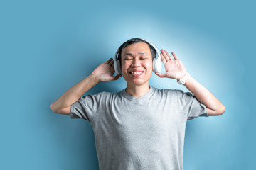 Asian man with headphones listening to music on isolated blue background