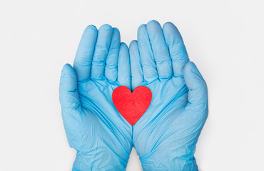 Fototapeta premium Hands in medical gloves holding a red heart shape model on white background. Cardiology. organ donation or Healthy heart concept