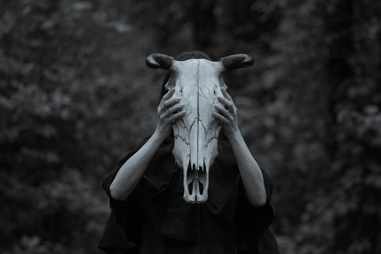Victim with skull of the animal instead of head. Photo stylized as shooting on an old camera, with noise and imperfection of the image. Woman in forest with skull of cow occupies Occult calls to demon