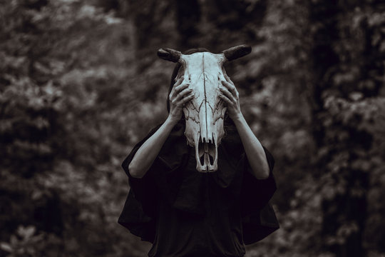 Victim with skull of the animal instead of head. Photo stylized as shooting on an old camera, with noise and imperfection of the image. Woman in forest with skull of cow occupies Occult calls to demon