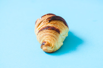 One croissant on a blue background, overhead view.