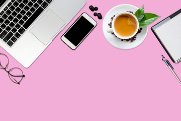 Top view of pink office desk table with laptop, smartphone, coffee cup, notebook, glasses with copy space.