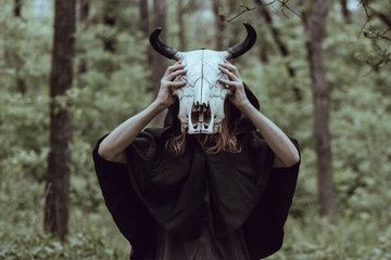 Naklejka premium Victim with skull of the animal instead of head. Photo stylized as shooting on an old camera, with noise and imperfection of the image. Woman in forest with skull of cow occupies Occult calls to demon