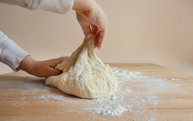 children's hands knead dough for home baking bread, pizza, pasta on the background of a wooden...