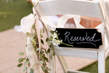 black reserved sign on chair at wedding ceremony with floral arrangement