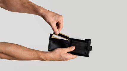 Young guy taking credit card out of wallet on light grey background, closeup. Panorama