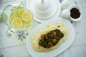 A bowl of white ceramic salt and pepper. Shah pilaf. Khan pilaf in a pita. Black pepper in a white ceramic pot . There is meat and plum chestnuts on the pilaf . Rice in a white plate. Sliced lemon .