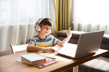 child boy  in headphones  show sight thumbs up, is using a laptop and communicates on the Internet ...