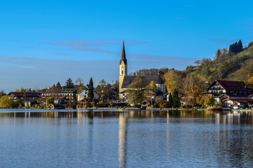 Fototapeta na wymiar Tegernsee in autumn with church reflection on water of lake ath the Alps of Germany near Munich